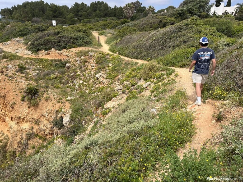 A person on a narrow dirt path on the trail of the headlands in the Algarve, Portugal.