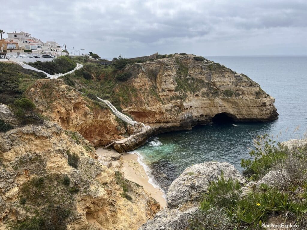 Tall limestone cliffs with white stairs leading to a beach along the trail of the headlands in the Algarve, Portugal.