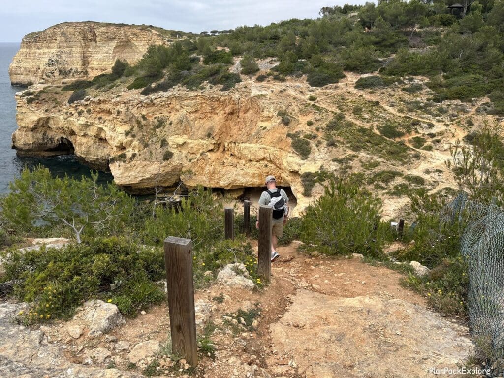A person on a downhill path marked with wooden posts, along the trail of the headlands in Portugal.