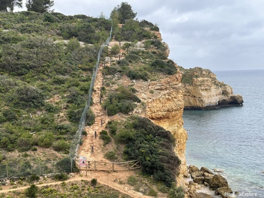 An uphill cliffside dirt path with a fence on the side on the trail of the headlands in Portugal.