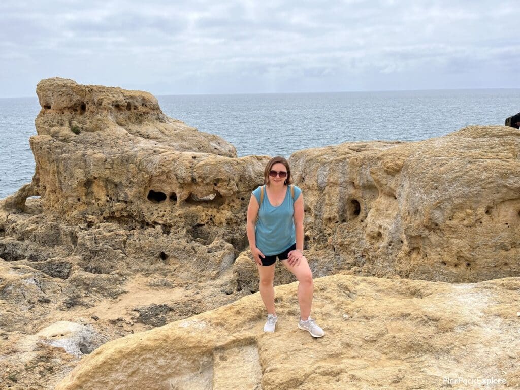 A person standing at the edge of a limestone cliff in the Algarve with more rock formations in the background.