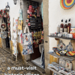 A shopfront in Óbidos, Portugal, displays a variety of handmade goods, including bags, toys, and ceramic items, highlighting the village's charm as a historic destination.