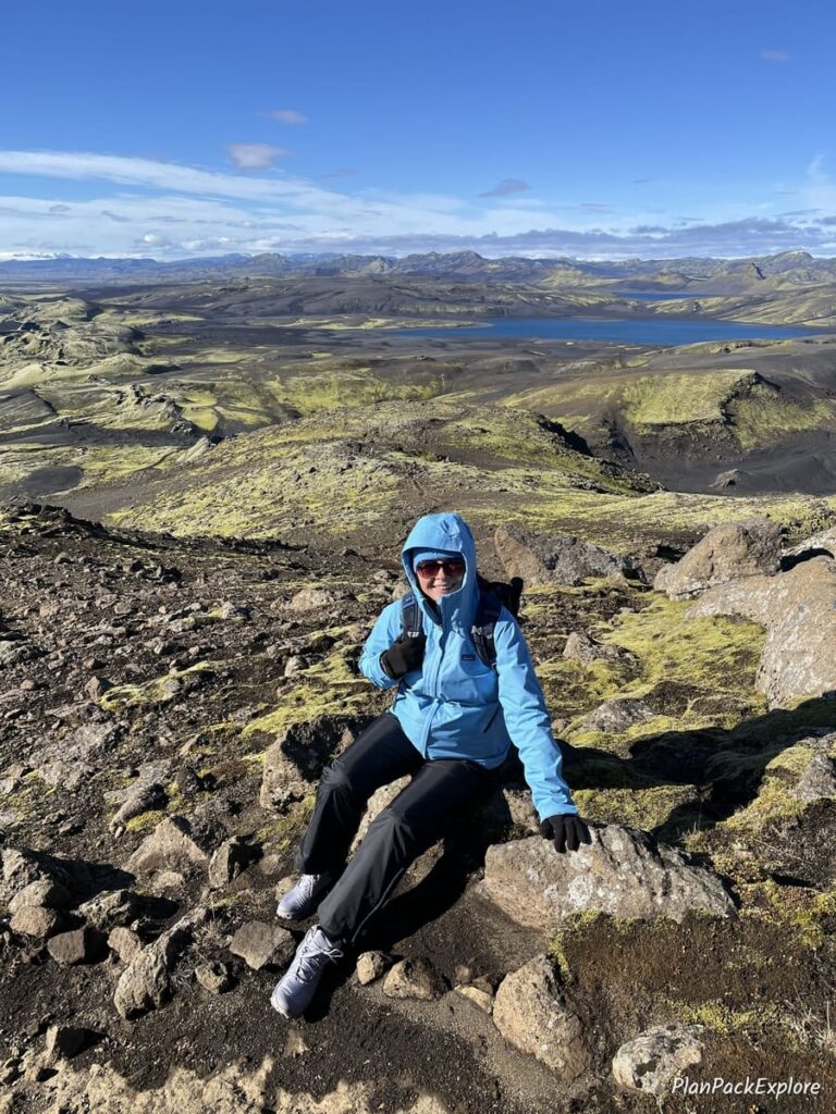 A person in a blue jacket sitting on a rock on a gravel path to Mount Laki in Iceland.