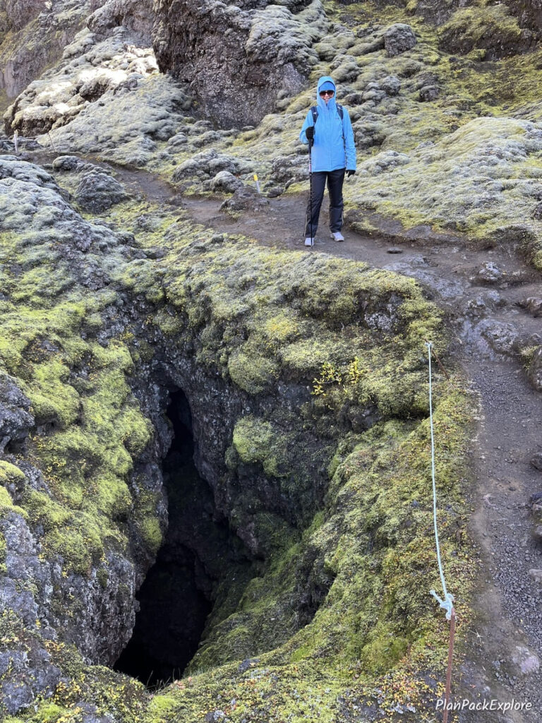 A person in a blue jacket on a gravel path next to a volcanic fissure in Laki, Iceland.
