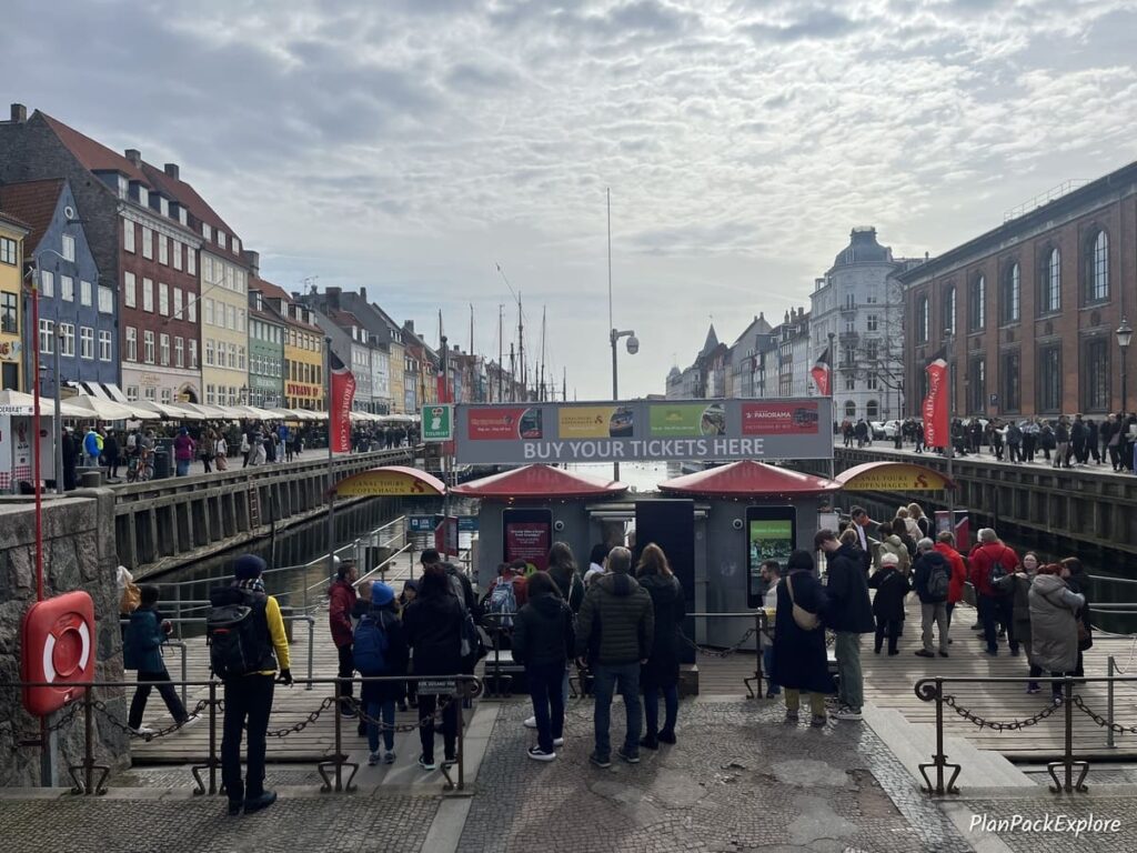 A large group of people standing by a ticket booth for canal boat tours in Copenhagen Denmark.