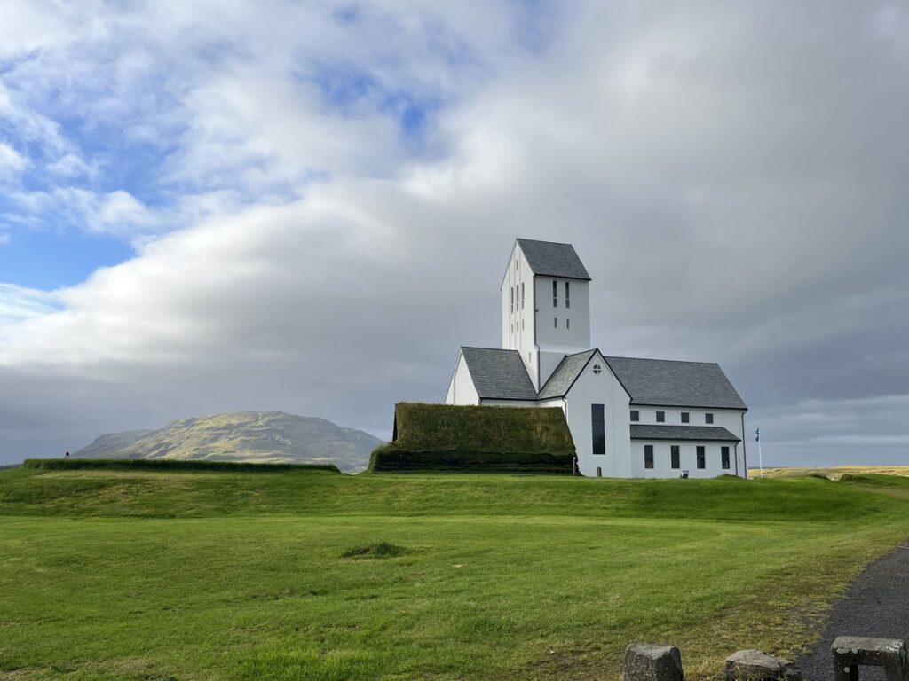 A white church called Skalholt Cathedral, with a turf house next to it in Iceland.