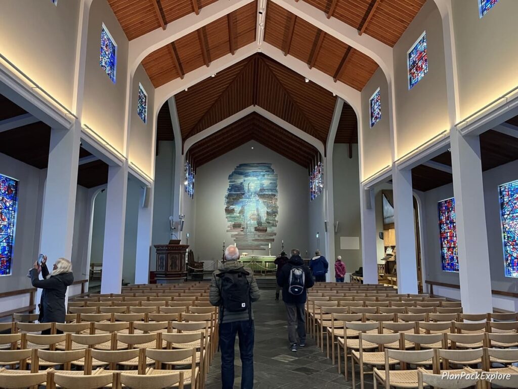 The inside of the church, called Skalholt Cathedral in Iceland, with wooden pews and roof, and a painted altar.