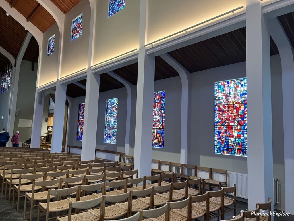 The inside of the church, called Skalholt Cathedral in Iceland, with wooden pews and colorful stained glass windows.