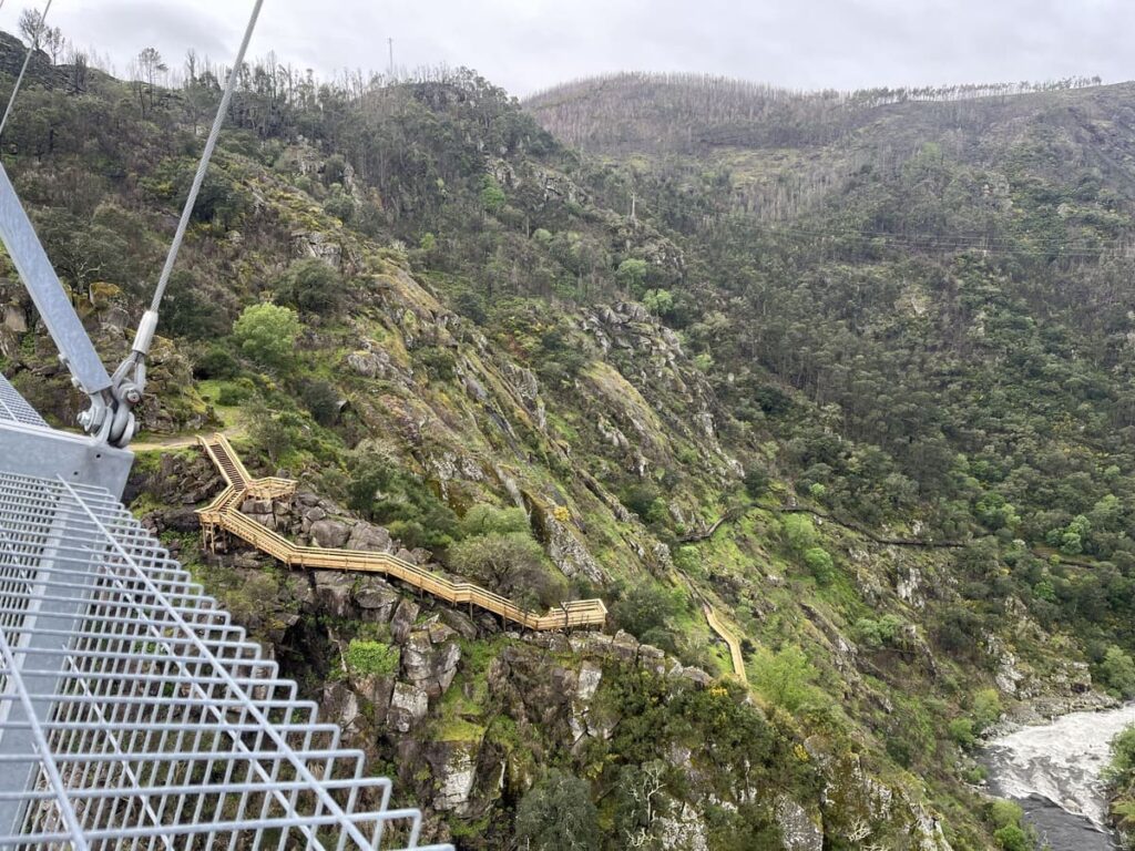 A wooden staircase next to a steel suspension bridge called 516 Arouca Bridge in Portugal.