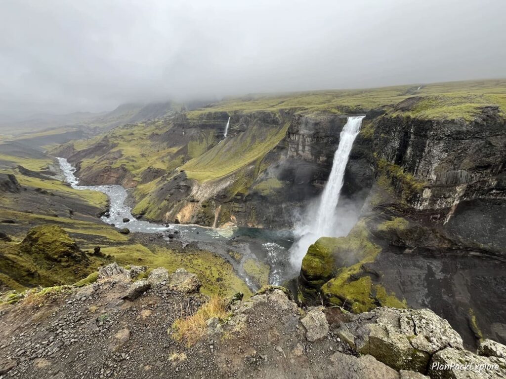 A waterfall cascading down a tall cliff in Thjorsardalur Valley, Iceland, with a river at the bottom.