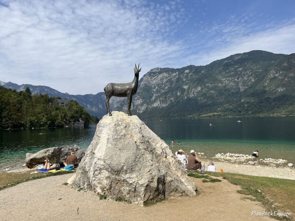 A statue of a goat called Zlatorog perched on a large rock, on the shore of lake Bohinj Slovenia