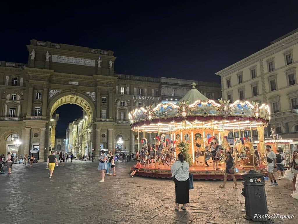 A plaza in Florence with a triumphal arch and a vintage carousel.