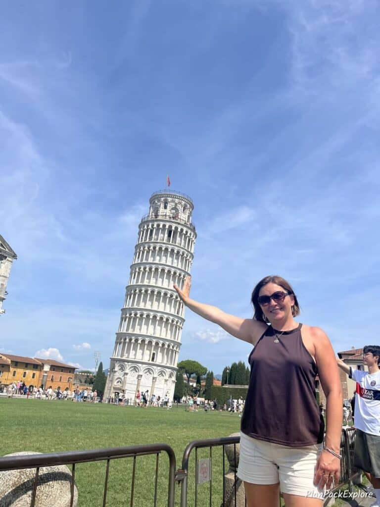 A woman extending her hand to imitate supporting the leaning tower of Pisa in Italy for a photo.