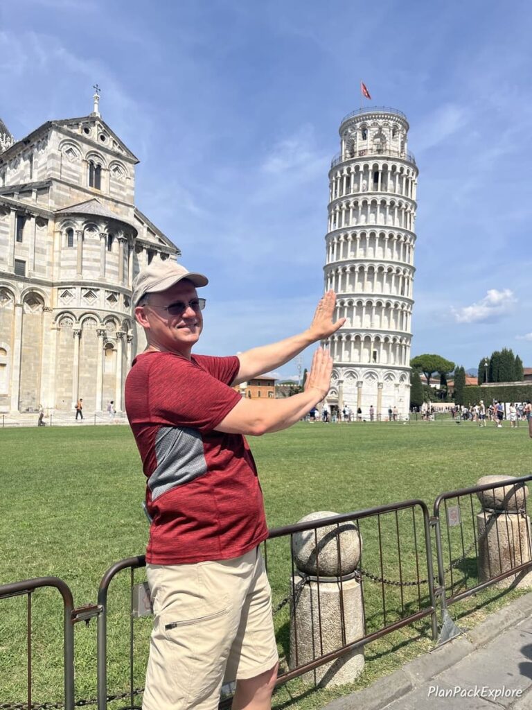 A man extending his hands to imitate supporting the leaning tower of Pisa in Italy for a photo.