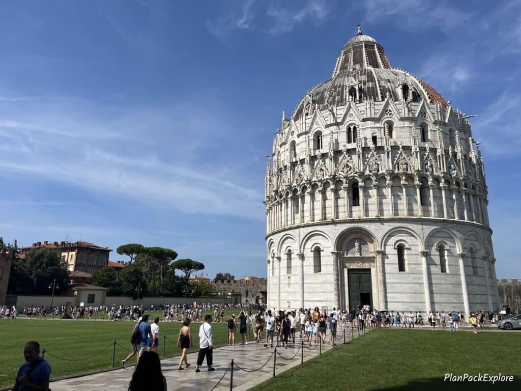 A white round building with a dome decorated with marble carvings, called the Baptistery in Pisa, Italy.
