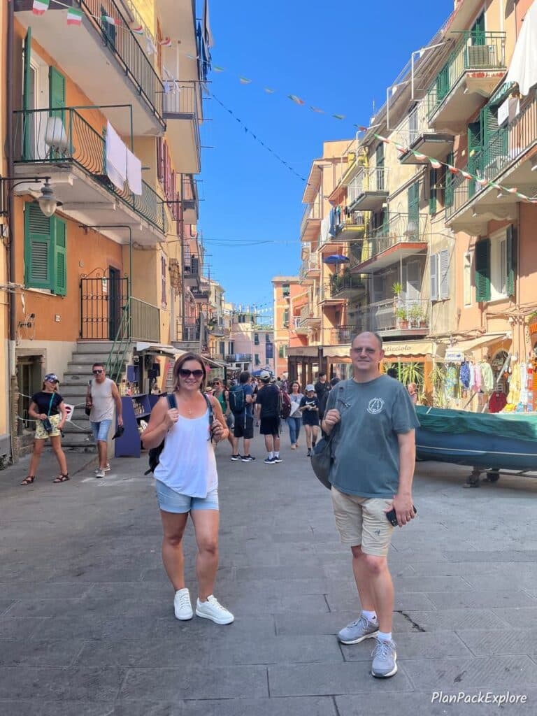 Two people standing in a colorful street with shops and cafes in Cinque Terre, Italy.