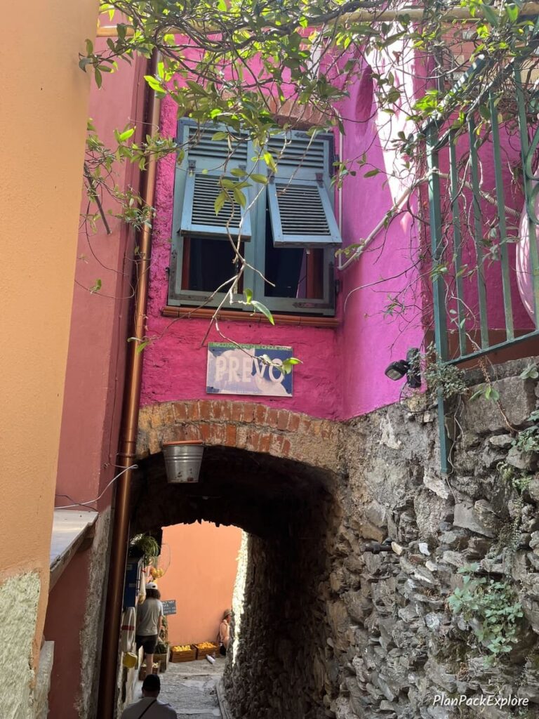 A narrow pink building and an archway with a sign "Prevo" on a trail in Cinque Terre, Italy.