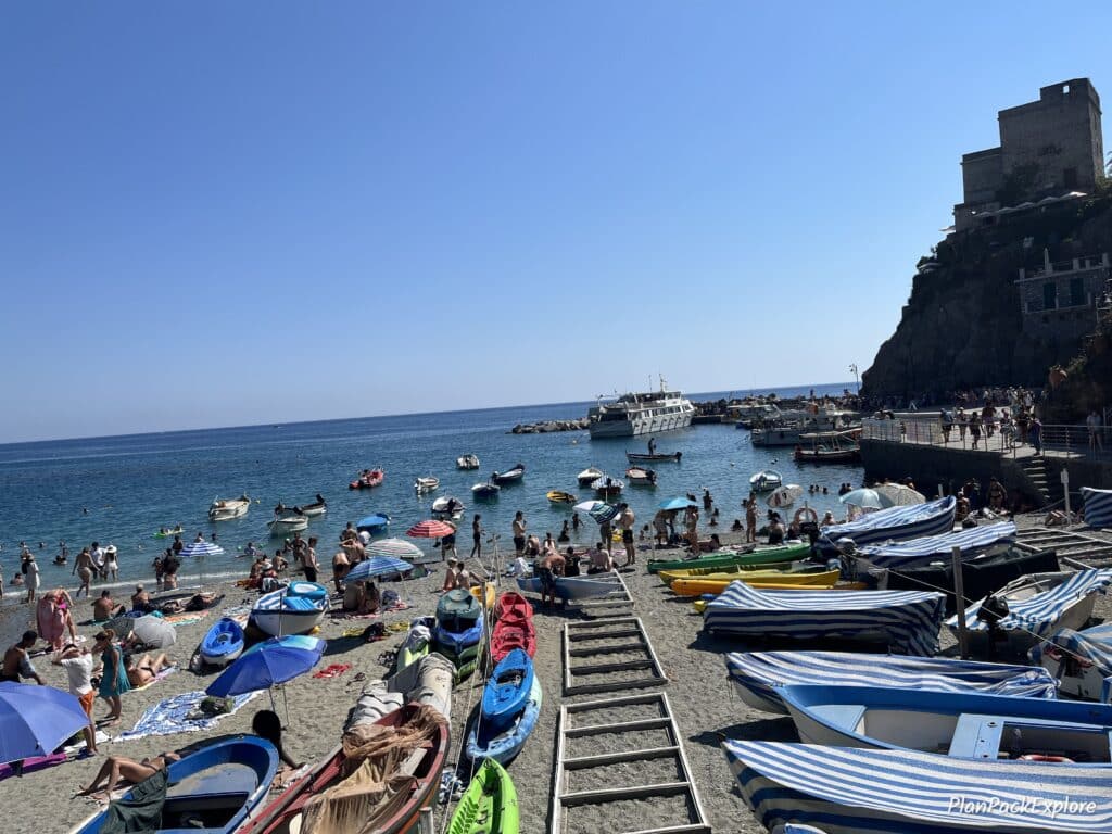 A sandy beach with boats, kayaks and people swimminh in the sea in the village of Monterosso al Mare, in Cinque Terre.