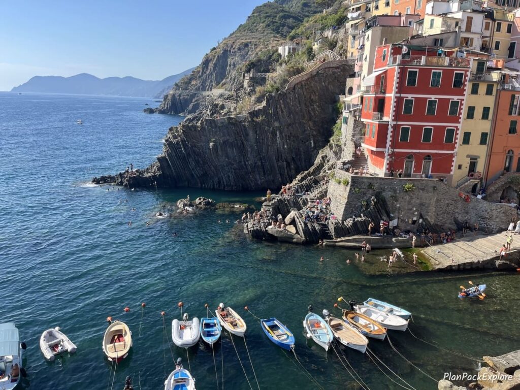 Colorful mountainside houses and a wooden dock and kayaks in the water, in Cinque Terre, Italy.