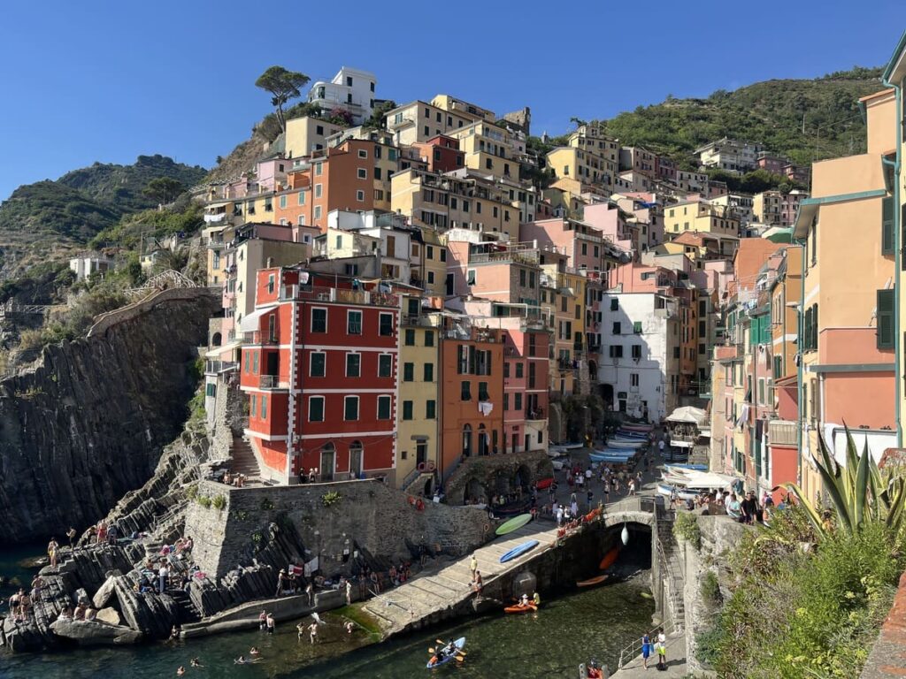 Colorful mountainside houses and a wooden dock and kayaks in the water, in Cinque Terre, Italy.