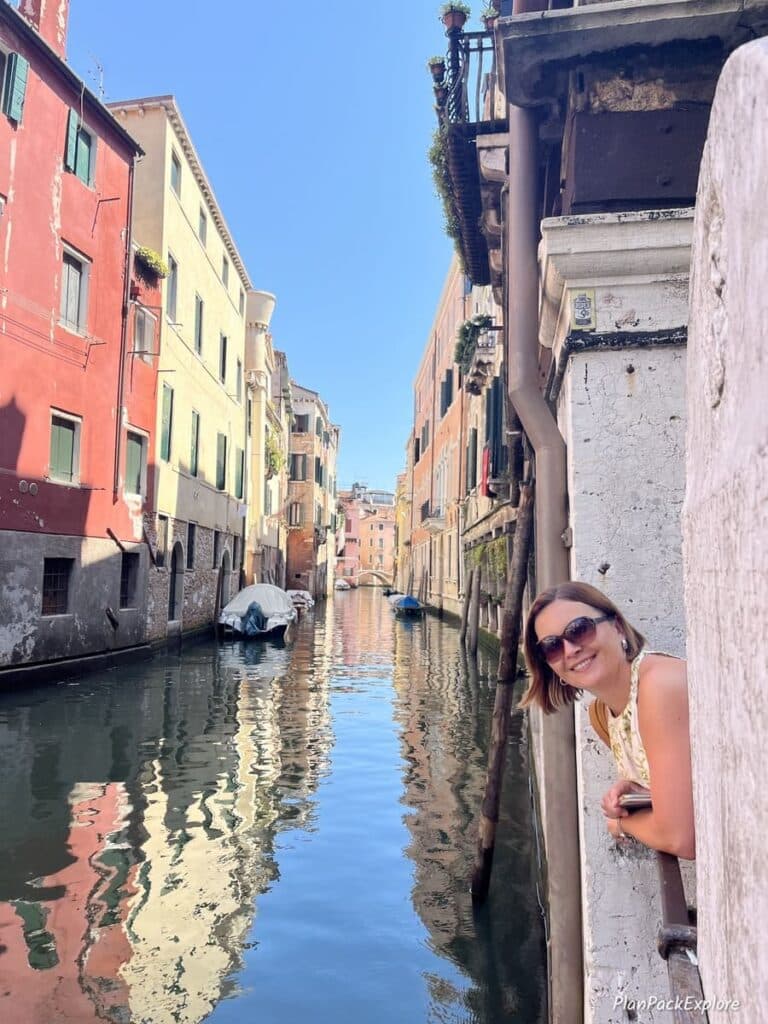A person peeking from behind a building near a canal in Venice, Italy.