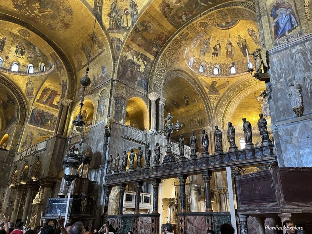 A view of the ceiling decorated with golden mosaics and a row of religious statues inside St. Mark's Basilica in Venice. A