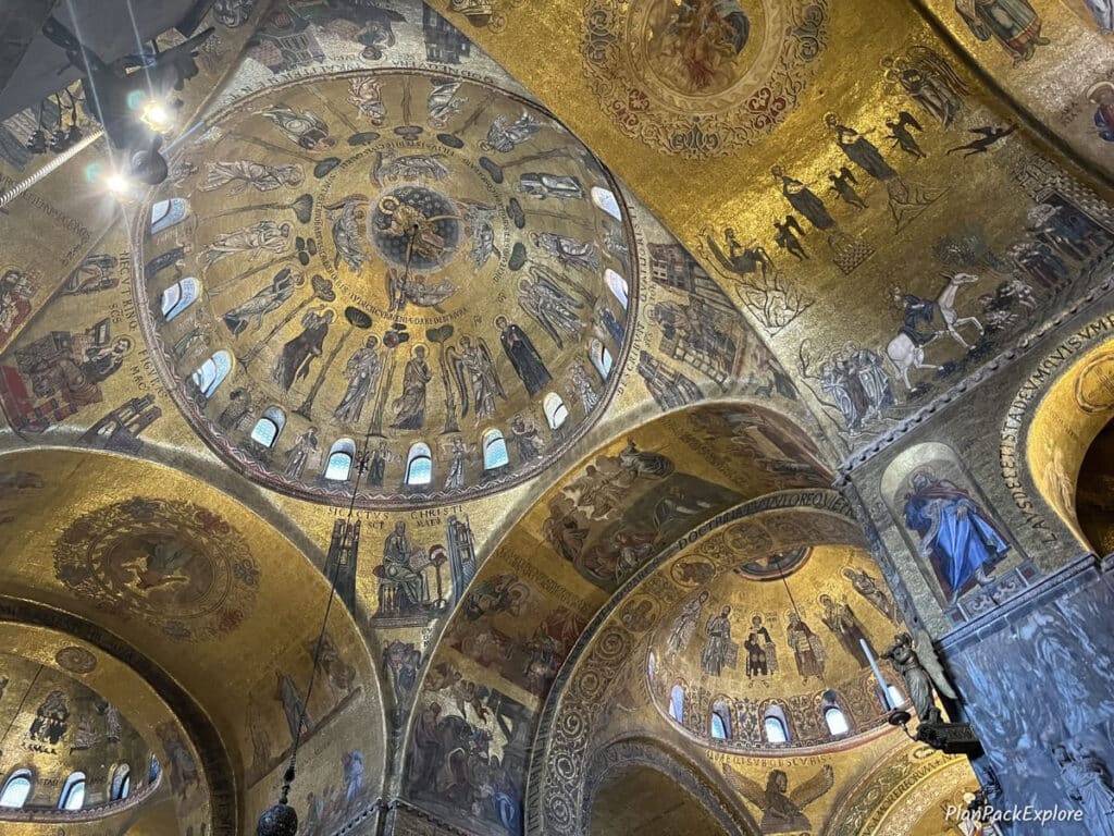 A domed ceiling decorated with golden mosaics inside St. Mark's Basilica in Venice. A