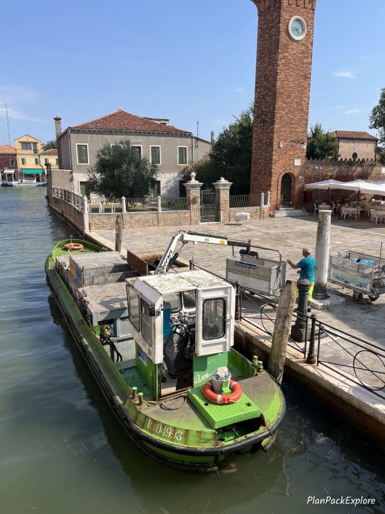 A boat collecting trash on a canal of a Venetian lagoon Island in Italy.