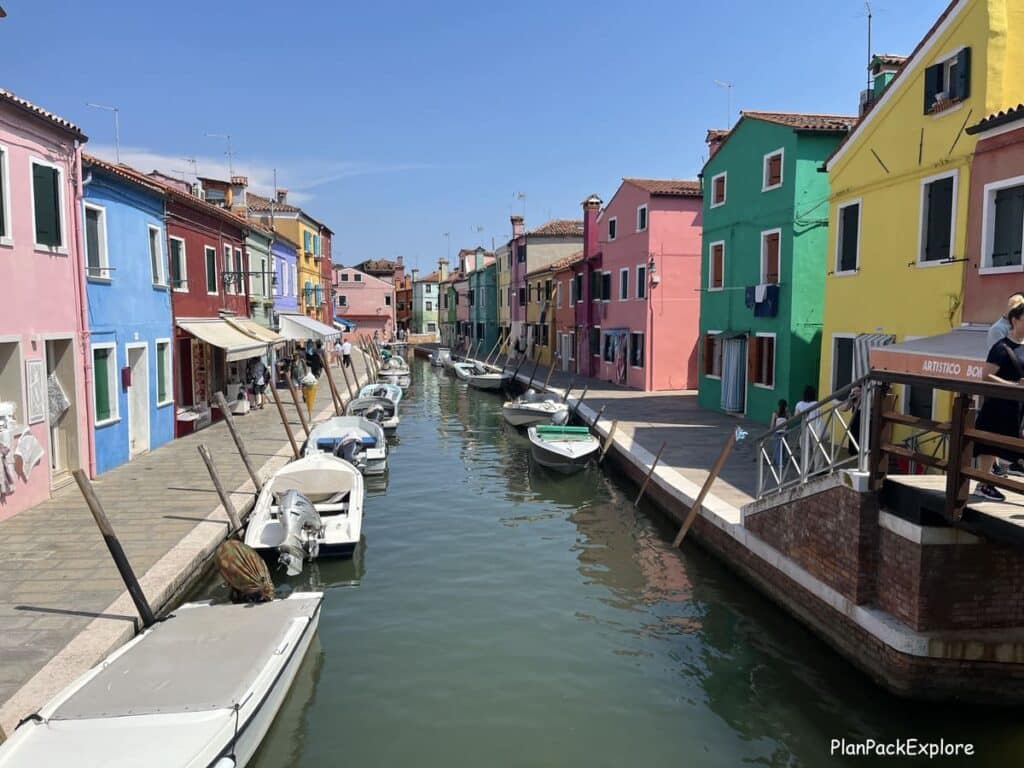A canal with boats and colorful, painted buildings on both sides on an island of Burano, near Venice, Italy.