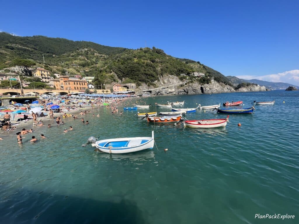 A view of the sea with boats and a beach with colorful umbrellas and pastel buildings in the background in Monterosso al Mare, Cinque Terre, Italy.