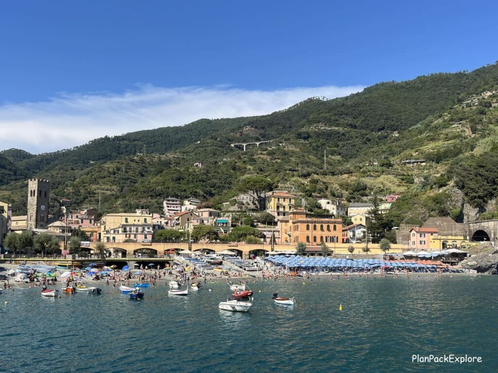 A view of the sea with boats and a beach with colorful umbrellas and pastel buildings in the background in Monterosso al Mare, Cinque Terre, Italy.