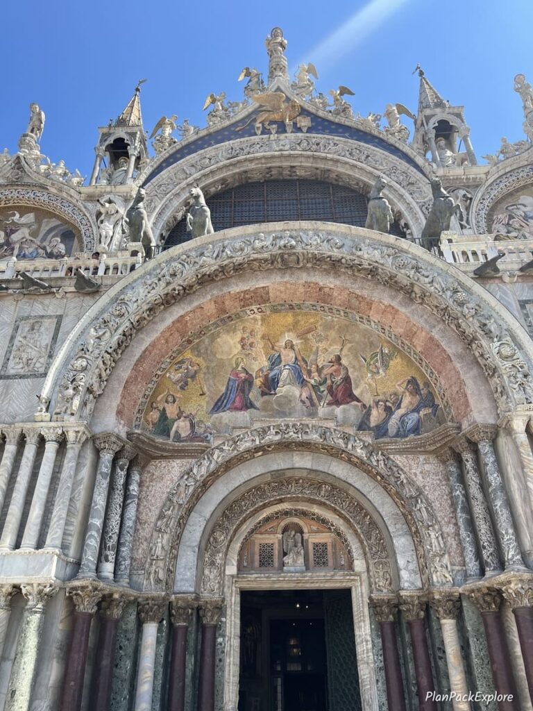 An ornate stone arch with paintings over an entry door to Basilica di San Marco in Venice, Italy.