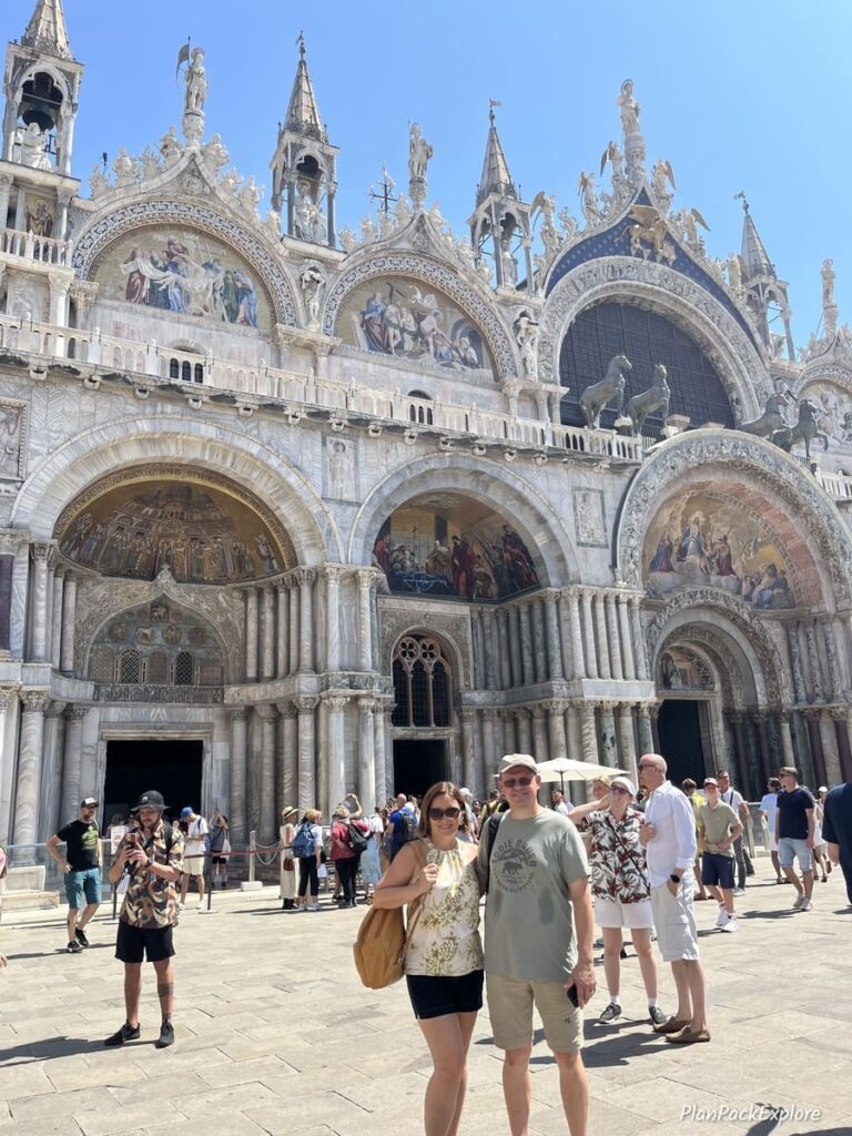 A couple standing in front of an ornate church in a busy square in Venice, Italy.