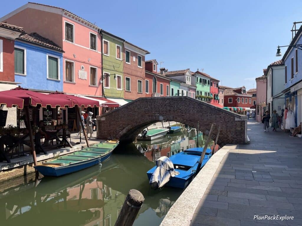 A busy street, colorful buildings and a bridge over the canal on Burano in Italy.