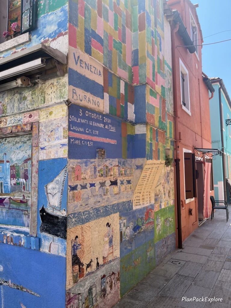 A close-up of a house painted with aquatic-themed murals and listing high tides, on Burano in Italy.