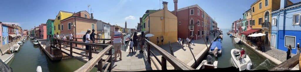 A panoramic view of a wooden bridge over three canals on Burano, Italy.