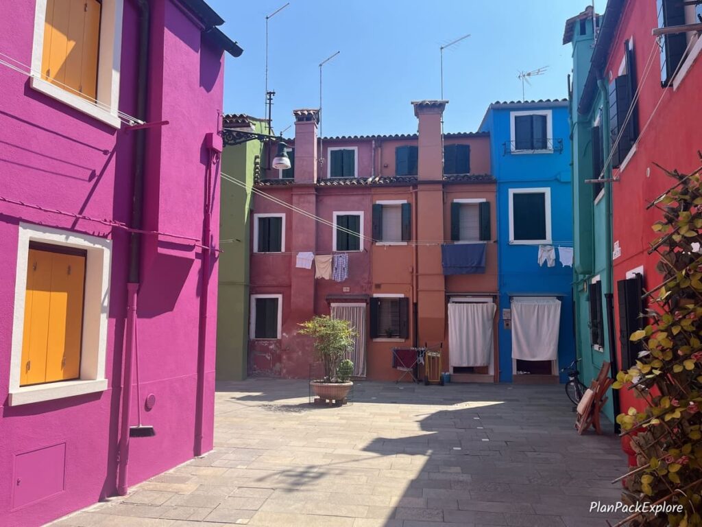 A small courtyard with bight colored houses and laundry hanging from the windows on Burano Island in Italy.