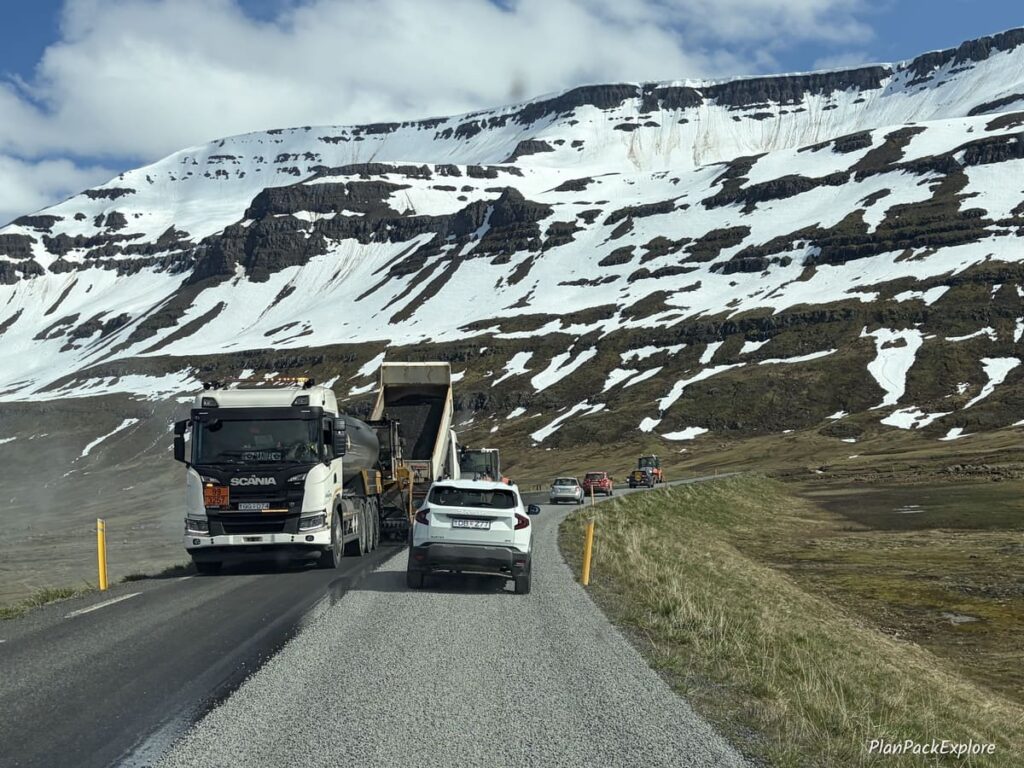 Cars and construction vehicles on a mountain road with a snow-covered peak in th e background in Seydisfjordur, Iceland.