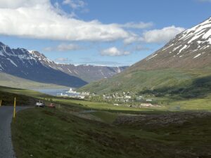 A view of a mountain road descending into the fjord with clear blue sky and colorful houses in the distance in Seydisfjordur, Iceland.