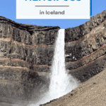 A view of Hengifoss waterfall cascading down rocky cliffs in Iceland, surrounded by a clear blue sky.