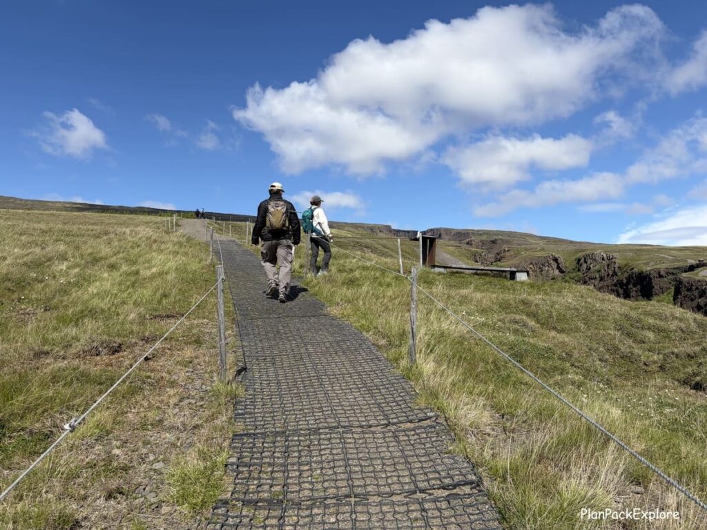 Two people are hiking on a trail to Hengifoss waterfall in East Iceland.