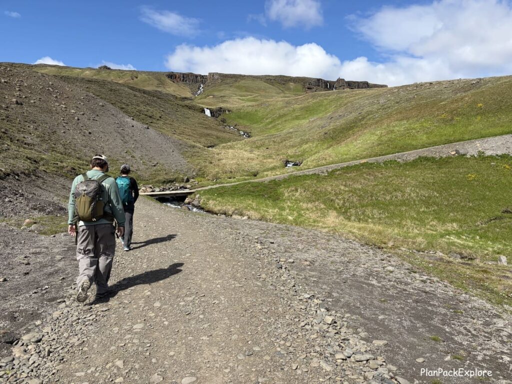 Two people hiking on a gravel path to Hengifoss waterfall in East Iceland.