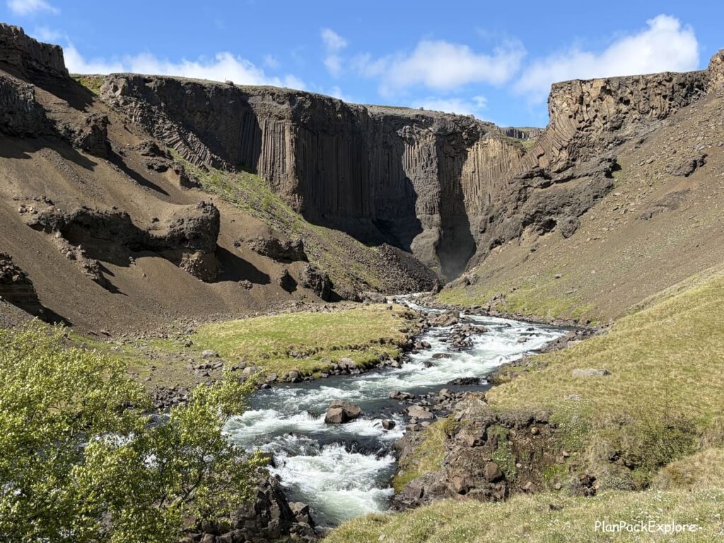 A view of a river and dark basalt cliffs on the trail to Hengifoss waterfall in Iceland.