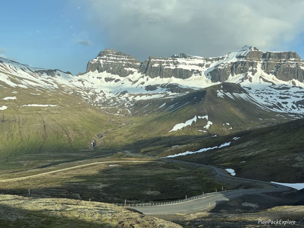 A winding road with snowy mountains in the background leading to Borgarfjordur Eystri in Iceland.