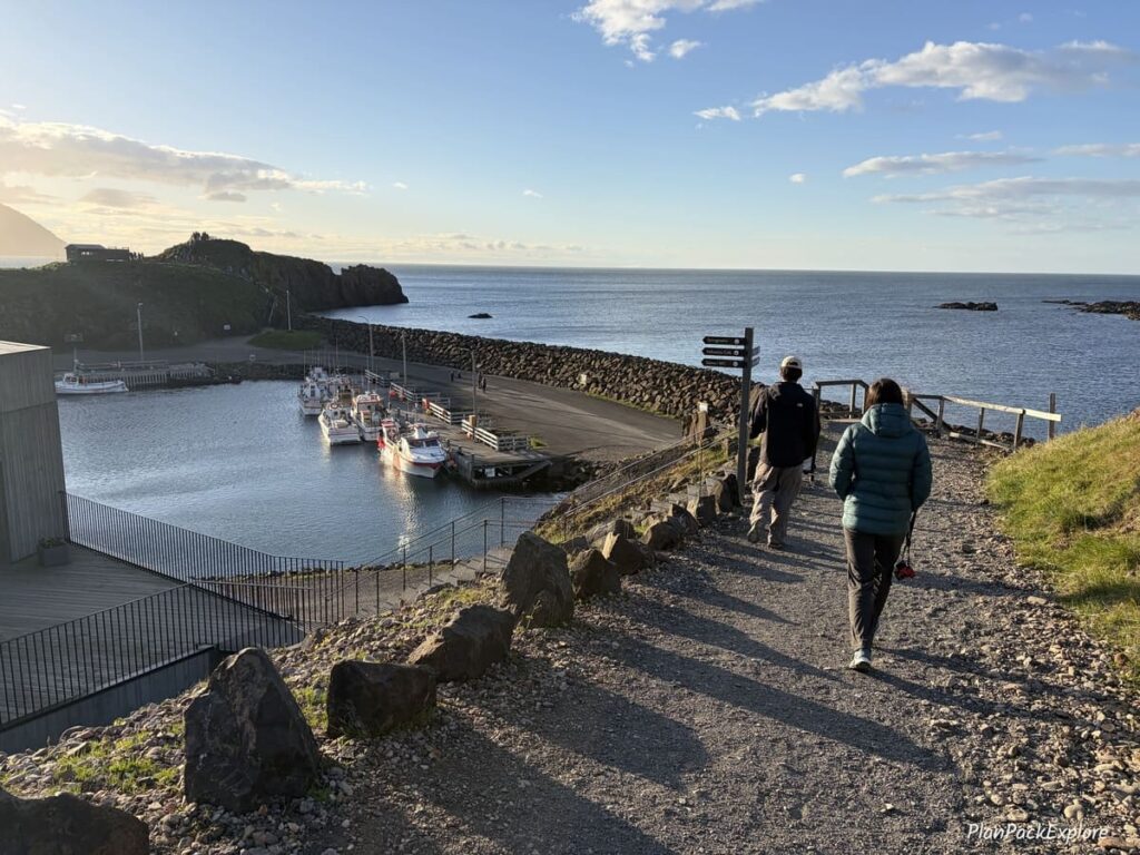 Two people walking on the gravel path towards wooden viewing platforms at Borgarfjordur Eystri in Iceland.