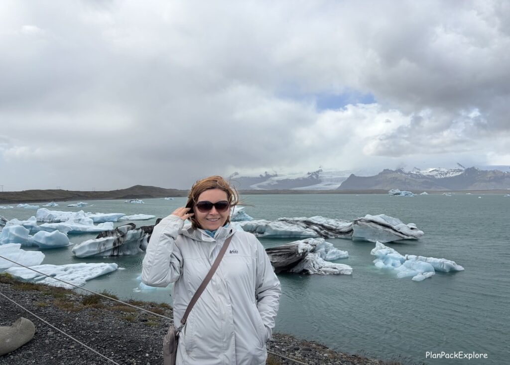 A person in a white jacket standing on the shore of a glacier lagoon in Iceland.
