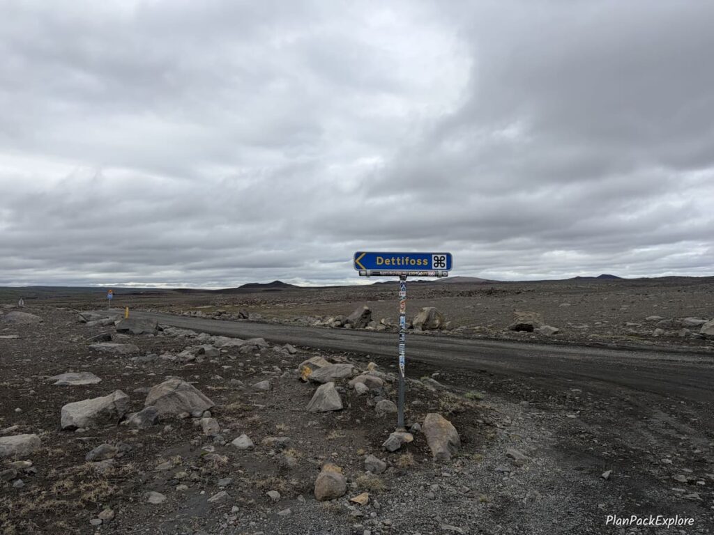 A blue sign on a gravel road marking the turn to Detifoss waterfall in Iceland.